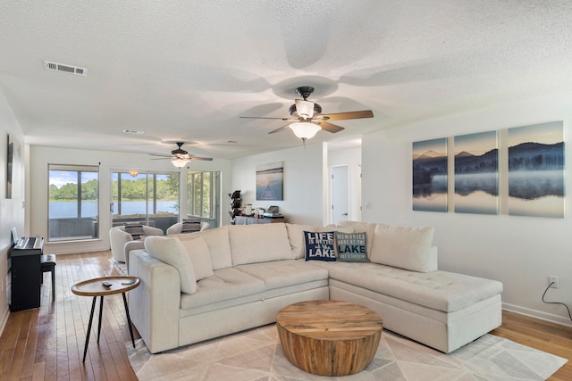 living room with a textured ceiling, a water view, light wood-type flooring, and ceiling fan