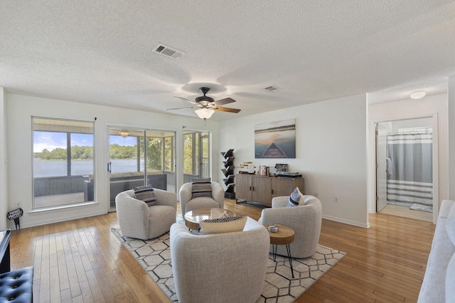 living room featuring light hardwood / wood-style floors, a water view, a textured ceiling, and ceiling fan