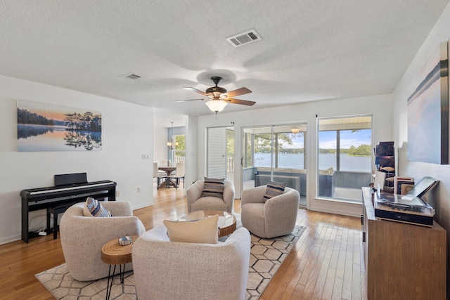 living room with ceiling fan, light wood-type flooring, and a textured ceiling