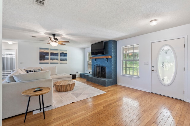 interior space with light hardwood / wood-style floors, a textured ceiling, a brick fireplace, brick wall, and ceiling fan