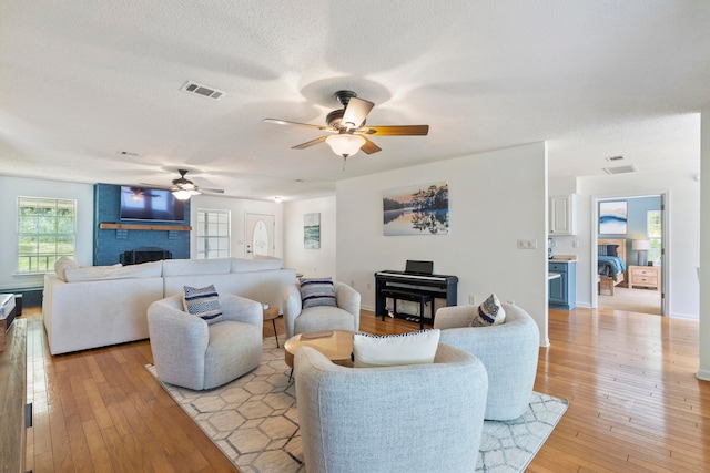 living room featuring a fireplace, light wood-type flooring, ceiling fan, and a textured ceiling