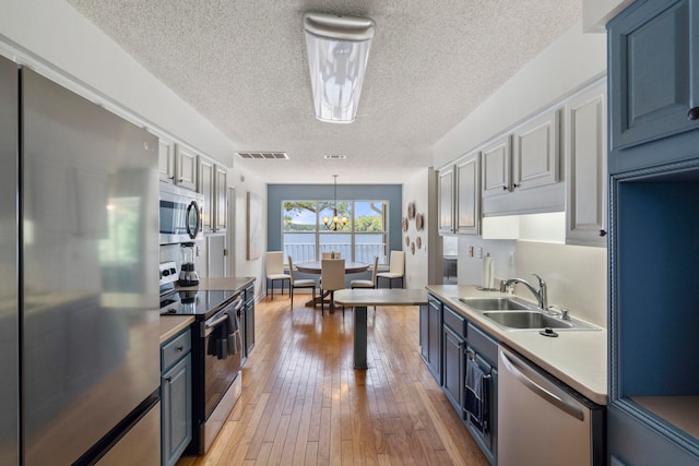 kitchen featuring light hardwood / wood-style flooring, a textured ceiling, stainless steel appliances, decorative light fixtures, and sink