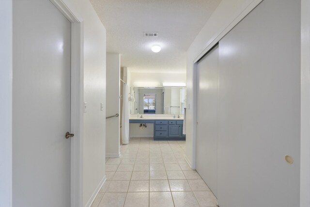 corridor featuring sink, a textured ceiling, and light tile patterned floors