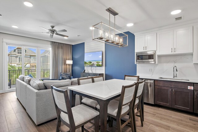 interior space with light wood-type flooring, ceiling fan with notable chandelier, sink, and crown molding