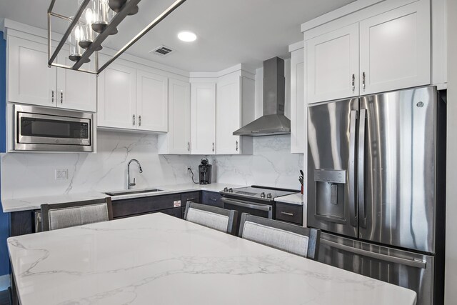 kitchen featuring backsplash, wall chimney exhaust hood, white cabinetry, appliances with stainless steel finishes, and light stone counters