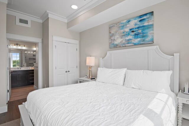 bedroom with dark wood-type flooring, a closet, sink, connected bathroom, and crown molding