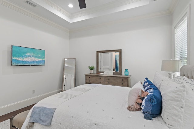 bedroom with a raised ceiling, visible vents, ornamental molding, wood finished floors, and baseboards