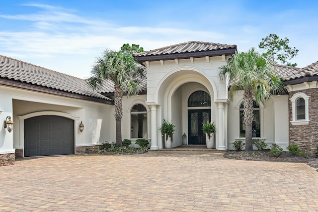 view of front facade featuring stone siding, french doors, decorative driveway, and stucco siding