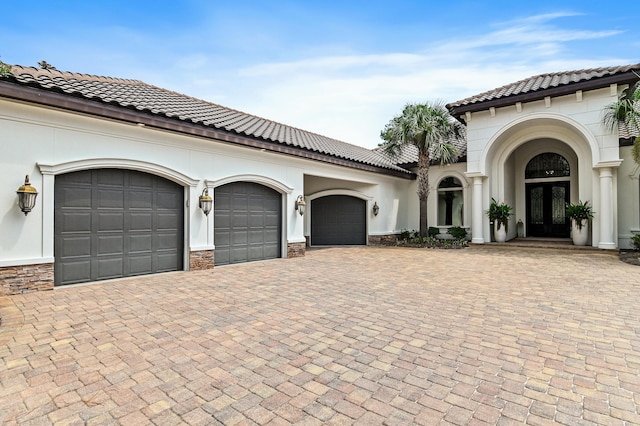 mediterranean / spanish house featuring an attached garage, stucco siding, decorative driveway, and french doors