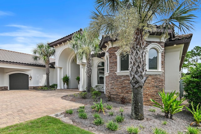 view of front of house featuring a garage, stone siding, a tiled roof, decorative driveway, and stucco siding