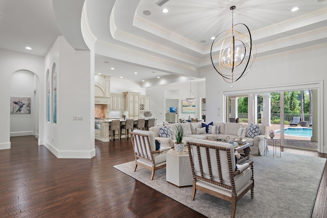 living room featuring dark wood finished floors, a raised ceiling, an inviting chandelier, ornamental molding, and baseboards