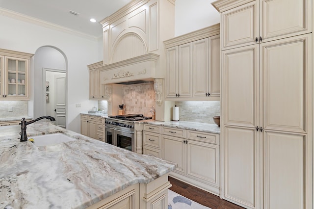 kitchen with arched walkways, cream cabinetry, range with two ovens, and a sink