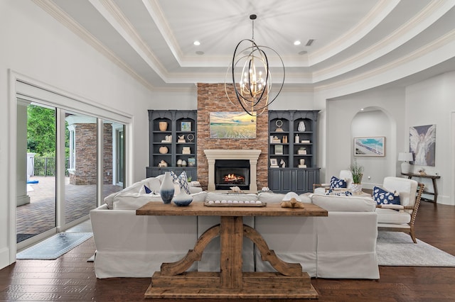 living area with built in features, a raised ceiling, dark wood-type flooring, crown molding, and a fireplace