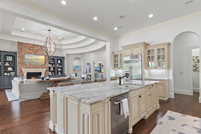 kitchen featuring arched walkways, dark wood-type flooring, stainless steel built in fridge, cream cabinets, and a sink