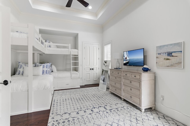 bedroom featuring ornamental molding, a tray ceiling, a ceiling fan, and wood finished floors