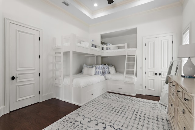 bedroom with a tray ceiling, visible vents, dark wood-type flooring, and ornamental molding