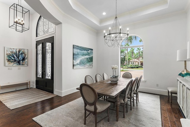 dining space with an inviting chandelier, a tray ceiling, and dark wood finished floors