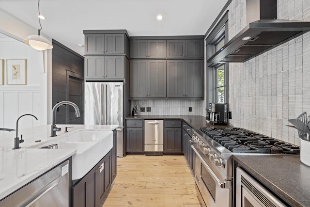 kitchen with decorative backsplash, light hardwood / wood-style floors, premium appliances, and wall chimney exhaust hood