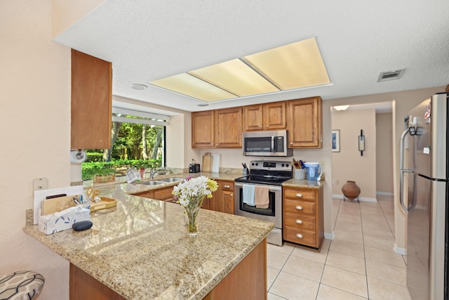 kitchen featuring visible vents, light stone counters, a peninsula, stainless steel appliances, and a sink