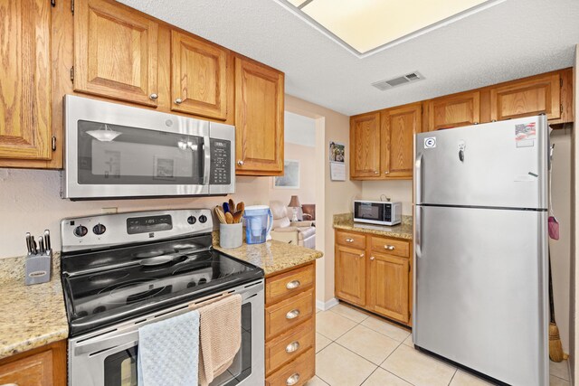 kitchen with appliances with stainless steel finishes, light stone counters, a textured ceiling, and light tile patterned floors