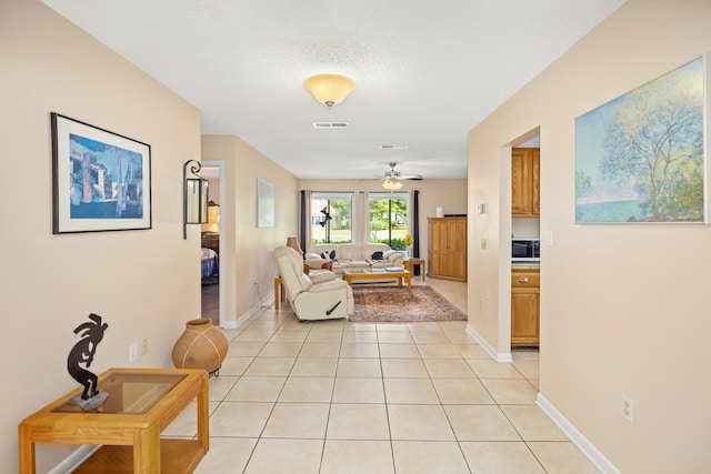 living area featuring visible vents, light tile patterned flooring, a textured ceiling, and baseboards