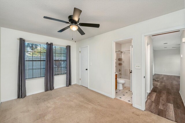 unfurnished bedroom with ceiling fan, a textured ceiling, connected bathroom, and light carpet