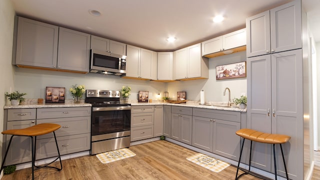 kitchen featuring light hardwood / wood-style floors, gray cabinets, a breakfast bar, sink, and stainless steel appliances