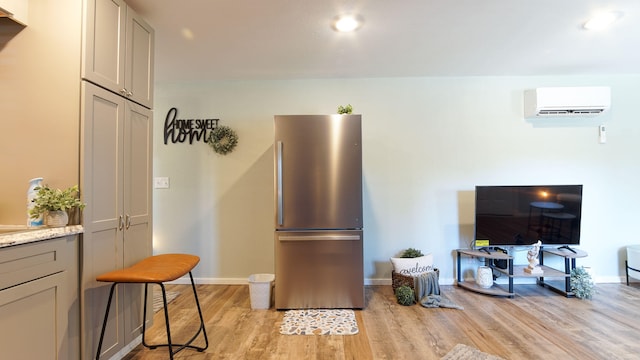 interior space with a wall mounted AC, gray cabinets, stainless steel refrigerator, light stone countertops, and light hardwood / wood-style floors