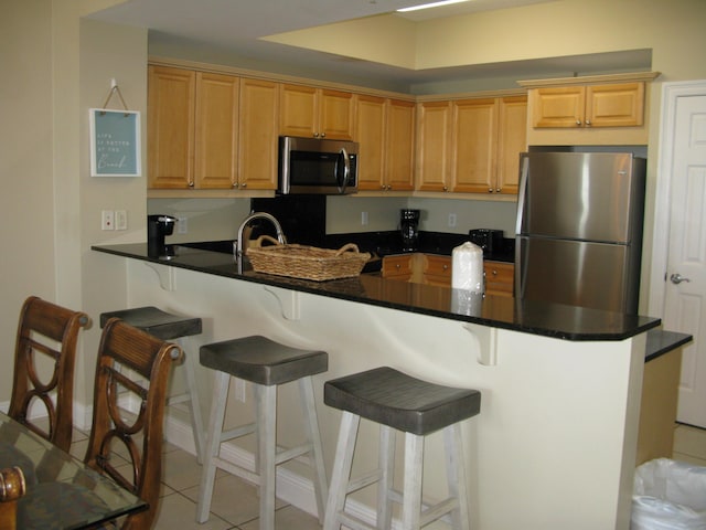 kitchen featuring a breakfast bar, light tile patterned flooring, kitchen peninsula, and appliances with stainless steel finishes