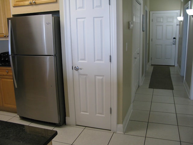 kitchen featuring dark stone countertops, light tile patterned floors, and stainless steel fridge