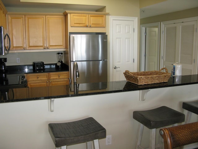 kitchen with stainless steel appliances, dark stone counters, a kitchen breakfast bar, and kitchen peninsula