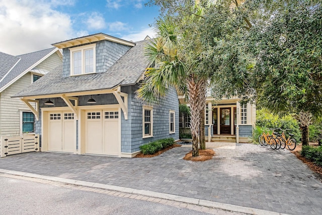 shingle-style home featuring decorative driveway, a garage, and roof with shingles