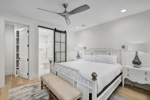 bedroom with light wood finished floors, visible vents, recessed lighting, and a barn door