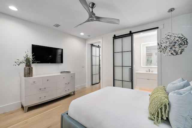 bedroom with visible vents, recessed lighting, a barn door, light wood-style floors, and baseboards