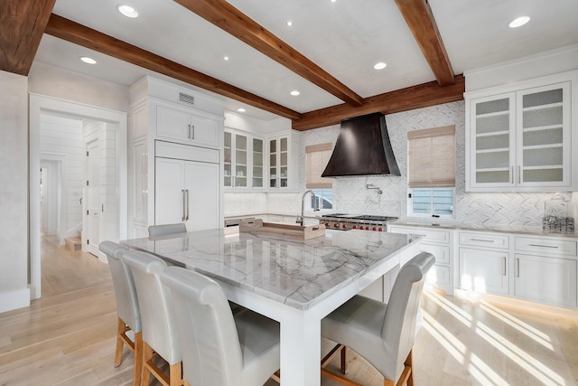 kitchen featuring premium range hood, paneled fridge, glass insert cabinets, range, and light stone countertops