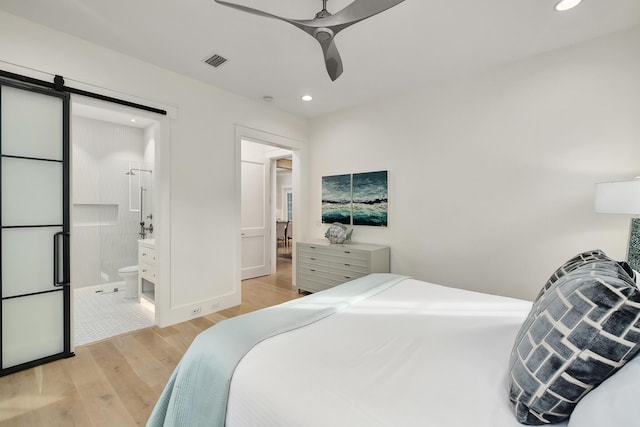 bedroom with a barn door, recessed lighting, light wood-style floors, and visible vents