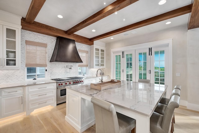 kitchen featuring luxury range, light wood-style flooring, custom range hood, white cabinets, and light stone countertops