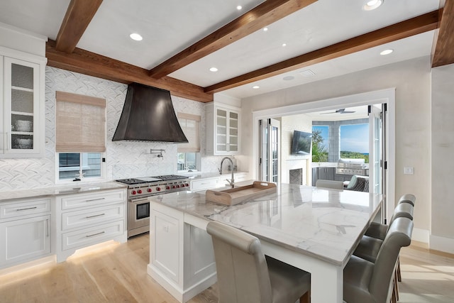 kitchen featuring light stone counters, custom exhaust hood, high end stove, white cabinets, and light wood-type flooring