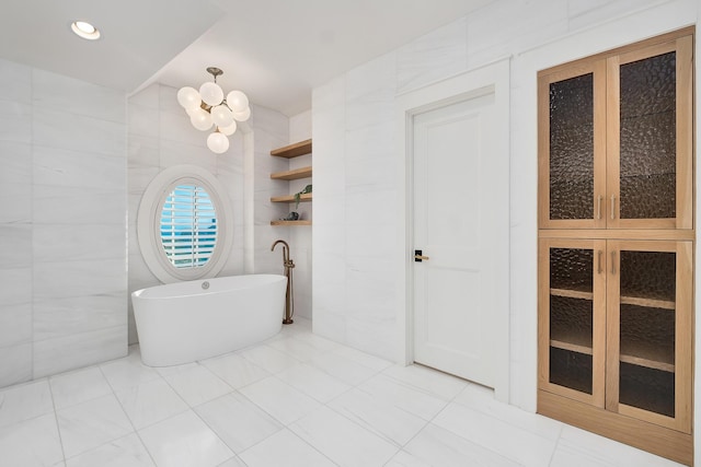 full bathroom with a notable chandelier, a soaking tub, and tile walls