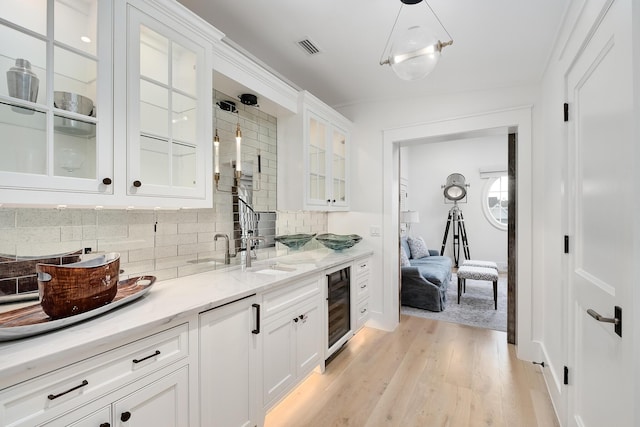 kitchen featuring visible vents, light stone countertops, beverage cooler, light wood-style floors, and white cabinetry