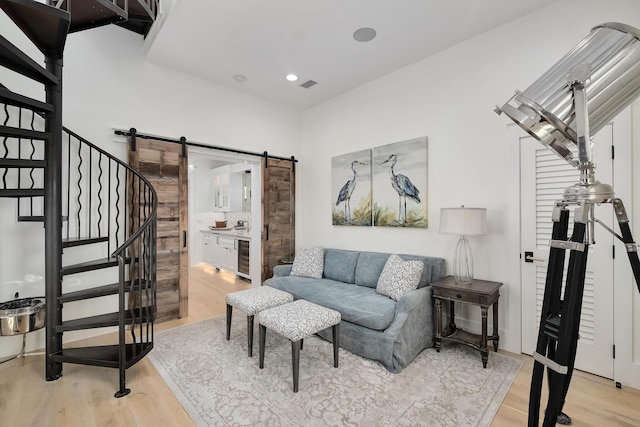 living room featuring visible vents, light wood-style flooring, a barn door, wine cooler, and stairs