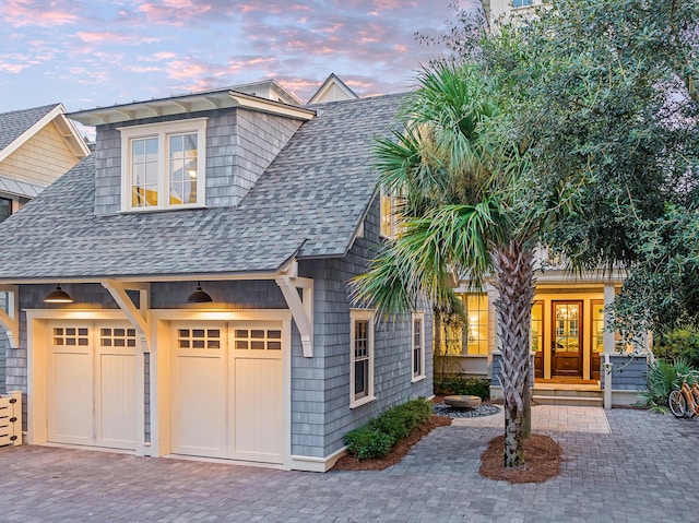 shingle-style home featuring decorative driveway, a garage, and a shingled roof