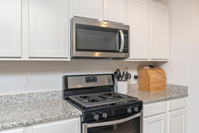 kitchen featuring light stone counters, stainless steel appliances, and white cabinets