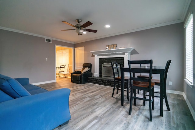 dining space featuring crown molding, ceiling fan, a stone fireplace, and hardwood / wood-style flooring