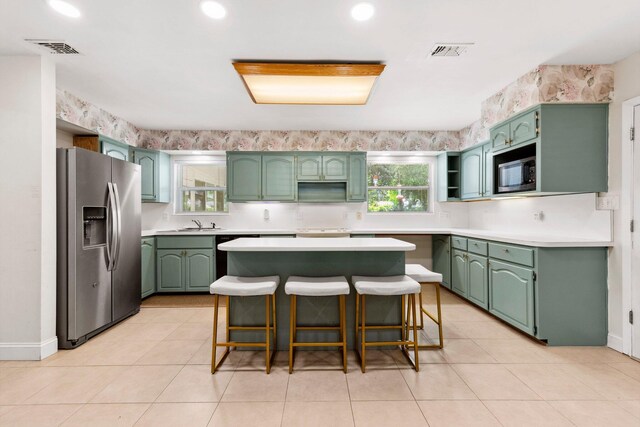 kitchen with light tile patterned floors, a center island, stainless steel appliances, and green cabinetry