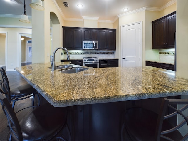 kitchen featuring visible vents, appliances with stainless steel finishes, a sink, dark stone countertops, and a kitchen bar