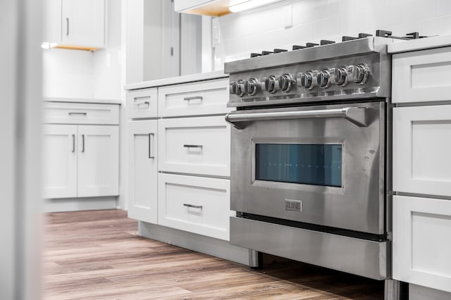 kitchen with tasteful backsplash, high end stainless steel range, light wood-type flooring, and white cabinetry