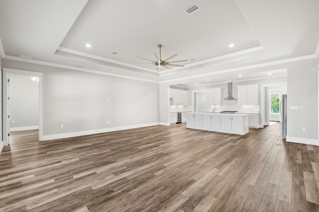 unfurnished living room featuring ornamental molding, ceiling fan, light hardwood / wood-style floors, and a raised ceiling