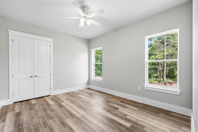 unfurnished bedroom featuring a closet, light hardwood / wood-style floors, multiple windows, and ceiling fan