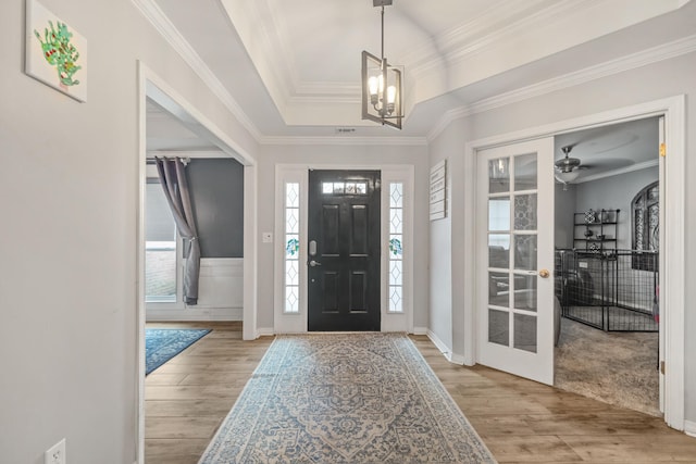 foyer with a tray ceiling, light hardwood / wood-style flooring, ceiling fan with notable chandelier, and ornamental molding